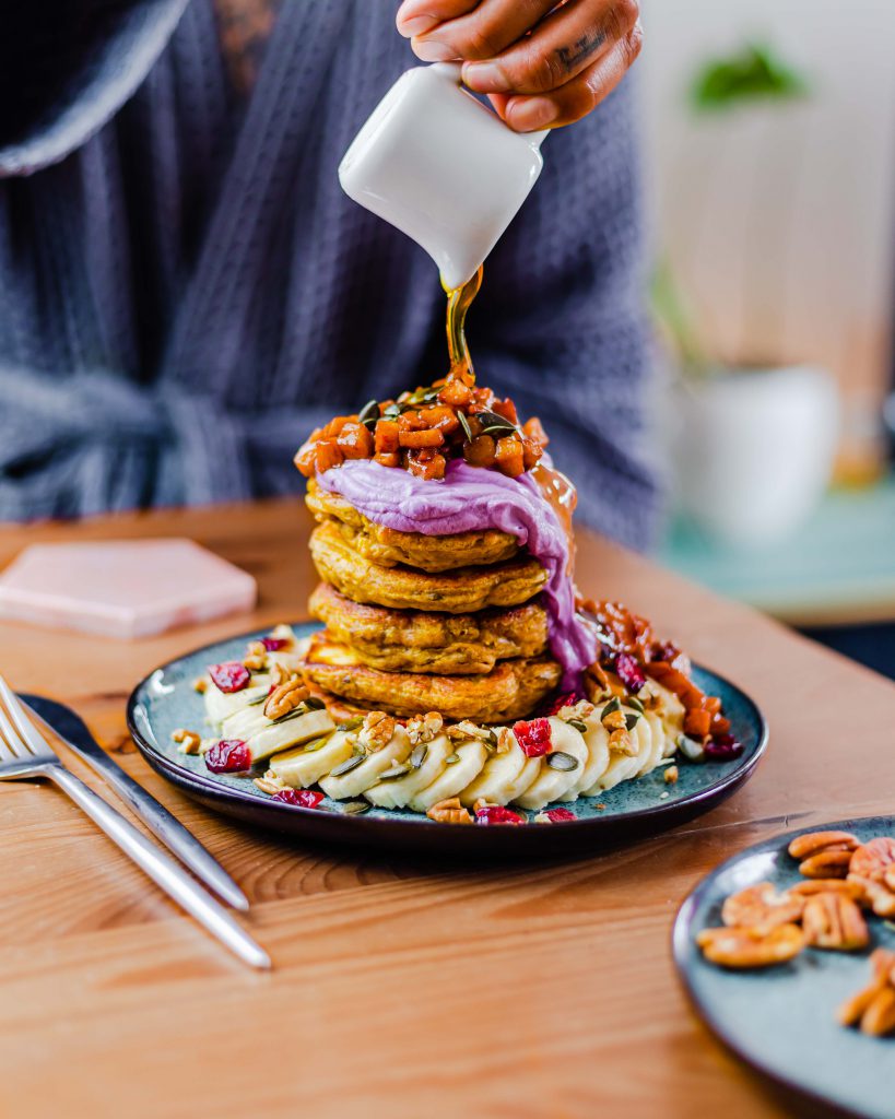 Pouring syrup on top of a stack of fluffy cinnamon apple pancakes