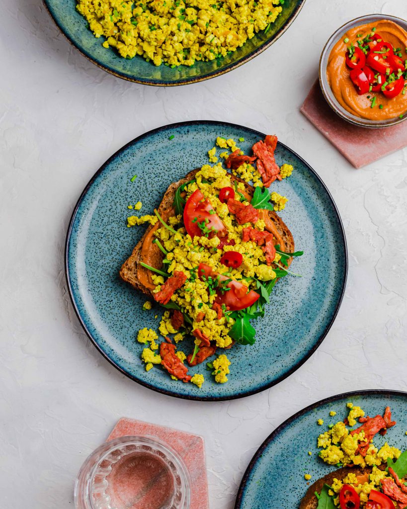 Toast with tofu scramble, arugula, tomato, chili peppers and vegan bacon.