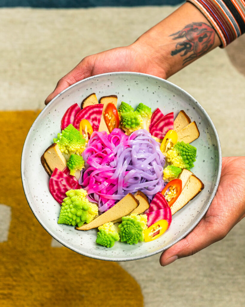 Me holding A bowl with colourful noodles, veggies and a creamy sauce